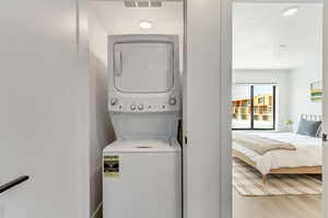 Washroom with stacked washer / drying machine and light wood-type flooring