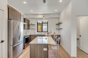 Kitchen with sink, a center island, stainless steel appliances, pendant lighting, and light hardwood / wood-style floors