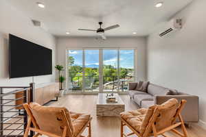 Living room with ceiling fan, light wood-type flooring, and an AC wall unit