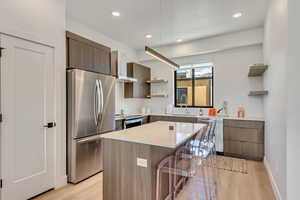 Kitchen with a center island, stainless steel appliances, wall chimney range hood, and light wood-type flooring