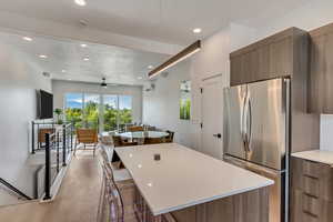 Kitchen featuring ceiling fan, stainless steel fridge, light wood-type flooring, a kitchen island, and a breakfast bar area
