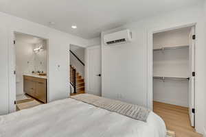Bedroom featuring a wall mounted AC, ensuite bath, and light hardwood / wood-style floors