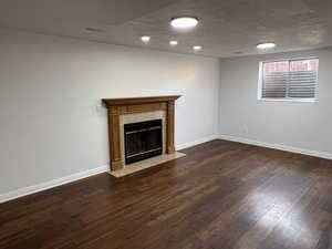 Unfurnished living room featuring dark wood-type flooring and a tiled fireplace