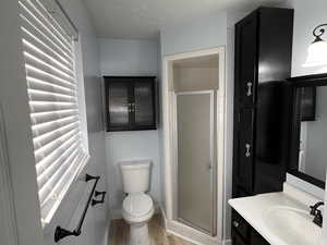 Bathroom with vanity, a textured ceiling, hardwood / wood-style flooring, toilet, and a shower with shower door