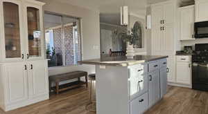 Kitchen featuring a kitchen bar, wood-type flooring, white cabinetry, and black appliances