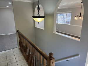 Hallway with a notable chandelier, ornamental molding, and light carpet