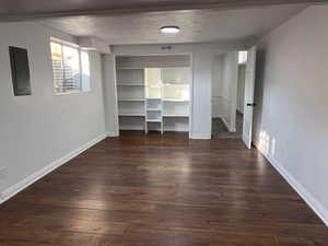 Unfurnished bedroom with a textured ceiling, electric panel, and dark wood-type flooring