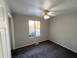 Unfurnished bedroom with ceiling fan and dark carpet