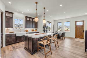 Kitchen with sink, backsplash, dark brown cabinets, a kitchen island, and light wood-type flooring