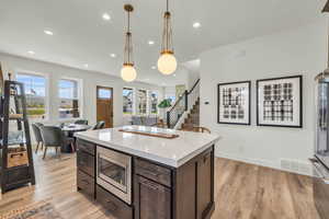 Kitchen with pendant lighting, dark brown cabinets, stainless steel microwave, and light wood-type flooring