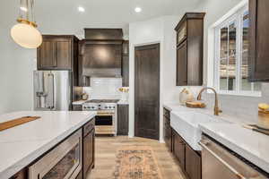 Kitchen featuring light stone countertops, sink, hanging light fixtures, high quality appliances, and light wood-type flooring