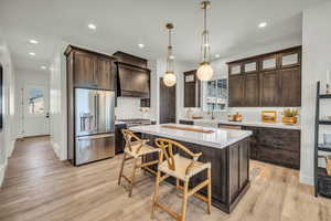 Kitchen featuring a center island, hanging light fixtures, light wood-type flooring, premium appliances, and dark brown cabinets