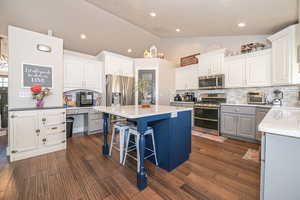 Kitchen with white cabinets, vaulted ceiling, decorative backsplash, a kitchen island, and stainless steel appliances