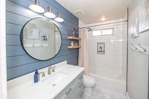 Full bathroom featuring shower / tub combo, vanity, toilet, and wooden walls