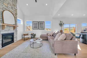 Living room with a stone fireplace, light hardwood / wood-style flooring, high vaulted ceiling, and a healthy amount of sunlight