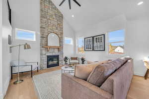 Living room featuring a fireplace, light wood-type flooring, high vaulted ceiling, and ceiling fan