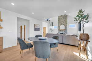 Dining room with a stone fireplace, light wood-type flooring, and vaulted ceiling