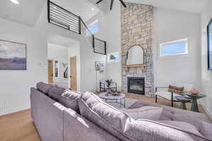 Living room featuring a stone fireplace, ceiling fan, light hardwood / wood-style flooring, and high vaulted ceiling