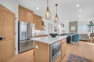 Kitchen featuring stainless steel appliances, pendant lighting, light brown cabinets, a center island, and light hardwood / wood-style floors