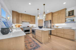 Kitchen with high end appliances, sink, hanging light fixtures, custom range hood, and light wood-type flooring