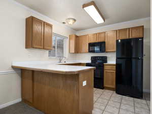 Kitchen featuring kitchen peninsula, light tile patterned floors, crown molding, and black appliances