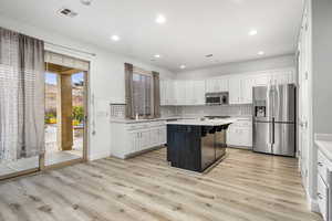 Kitchen featuring stainless steel appliances, a kitchen island, white cabinetry, and light hardwood / wood-style floors