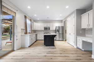 Kitchen featuring sink, stainless steel appliances, a kitchen island, light hardwood / wood-style floors, and white cabinets