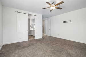 Unfurnished bedroom featuring light carpet, ensuite bathroom, sink, ceiling fan, and a barn door