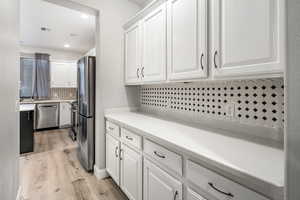 Kitchen featuring white cabinets, light hardwood / wood-style floors, appliances with stainless steel finishes, and tasteful backsplash