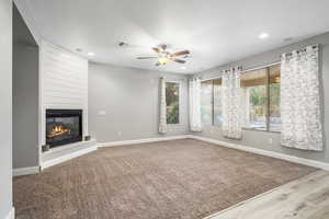 Unfurnished living room featuring ceiling fan, a large fireplace, and carpet floors