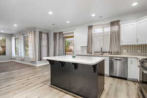 Kitchen featuring white cabinetry, a center island, stainless steel appliances, light hardwood / wood-style floors, and a breakfast bar