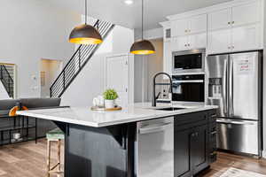 Kitchen featuring stainless steel appliances, pendant lighting, wood-type flooring, a center island with sink, and white cabinetry