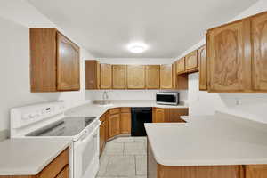 Kitchen with kitchen peninsula, sink, light tile patterned floors, dishwasher, and white range with electric cooktop