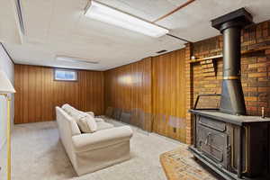 Living room featuring light colored carpet, a wood stove, and wooden walls