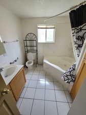 Full bathroom with vanity, tile patterned flooring, toilet, shower / bath combo with shower curtain, and a textured ceiling