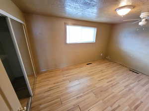 Unfurnished bedroom featuring ceiling fan, a closet, a textured ceiling, and light wood-type flooring