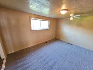 Empty room featuring a textured ceiling, carpet floors, and ceiling fan