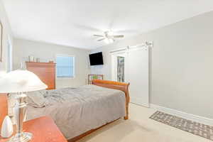 Carpeted bedroom with ceiling fan, a barn door, a walk in closet, and a closet