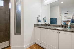 Bathroom with a tile shower, ceiling fan, hardwood / wood-style floors, and vanity