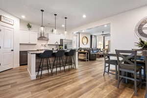 Kitchen featuring stainless steel refrigerator with ice dispenser, light wood-type flooring, a kitchen island with sink, white cabinets, and a breakfast bar area