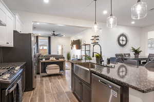 Kitchen with dark stone counters, white cabinets, hanging light fixtures, appliances with stainless steel finishes, and wood-type flooring