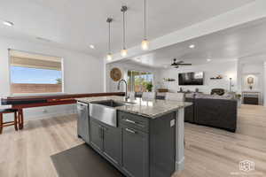 Kitchen with light stone counters, light hardwood / wood-style floors, a kitchen island with sink, ceiling fan, and gray cabinets