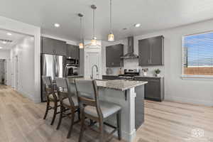 Kitchen with a center island with sink, wall chimney range hood, sink, light wood-type flooring, and appliances with stainless steel finishes