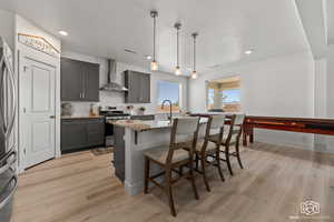 Kitchen with gas range, hanging light fixtures, wall chimney exhaust hood, and gray cabinetry