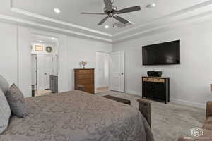 Carpeted bedroom with ceiling fan, connected bathroom, and a tray ceiling