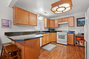 Kitchen with white range, light hardwood / laminate flooring, granite countertops, kitchen peninsula, and a breakfast bar area