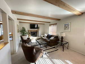 Living room featuring a stone fireplace, light colored carpet, and beam ceiling