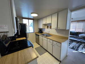 Kitchen featuring refrigerator, stainless steel dishwasher, sink, white cabinets, and black electric range oven