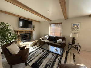 Carpeted living room featuring a stone fireplace and beamed ceiling