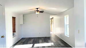 Empty room with a barn door, ceiling fan, dark wood-type flooring, and vaulted ceiling